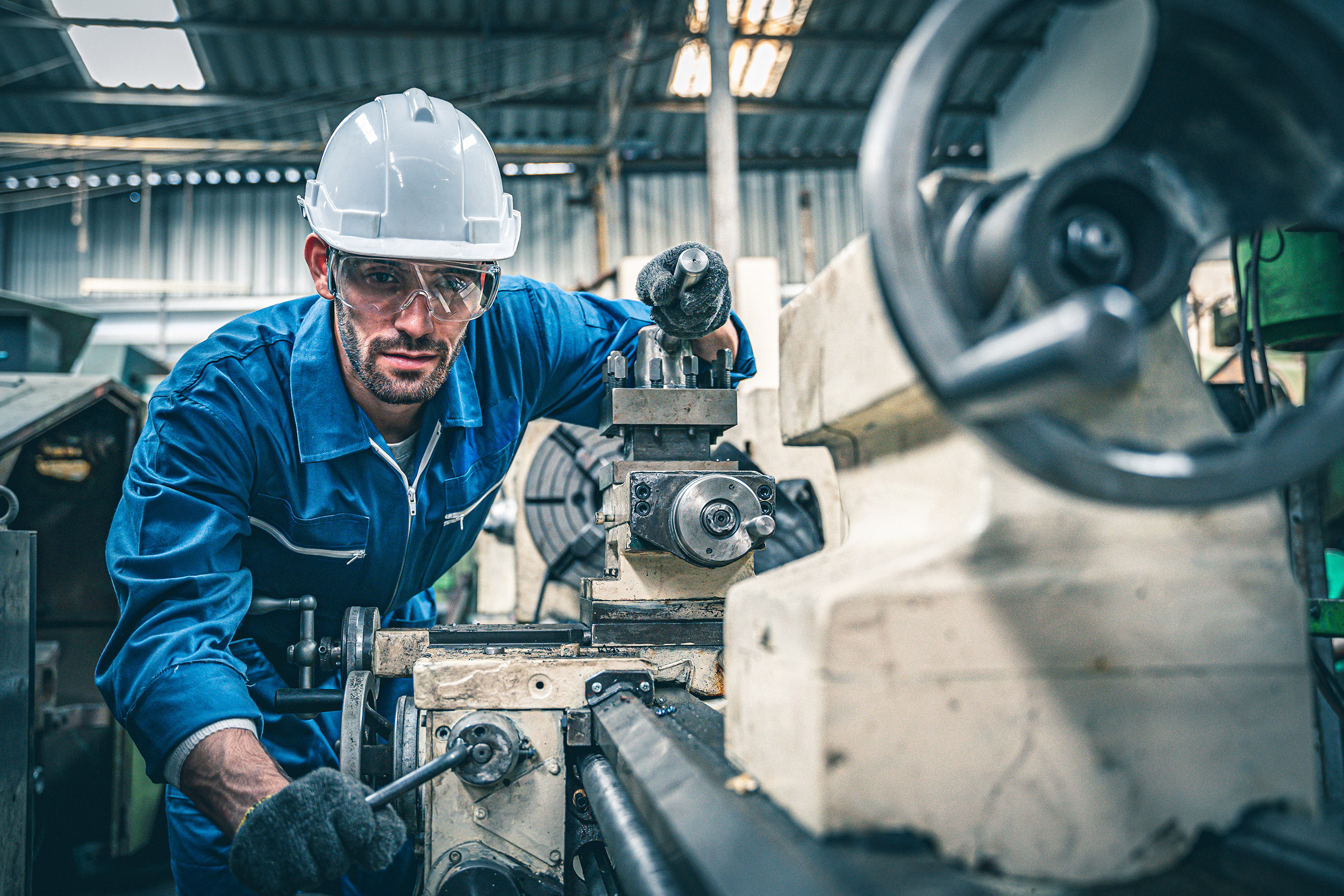Male worker in blue jumpsuit and white hardhat operating lathe machine Male worker in blue jumpsuit and white hardhat operating lathe machine